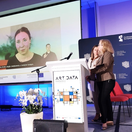 Two people standing on stage, a film showing in the distance