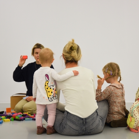 A woman and two girls are sitting on the floor and listening to a lecture