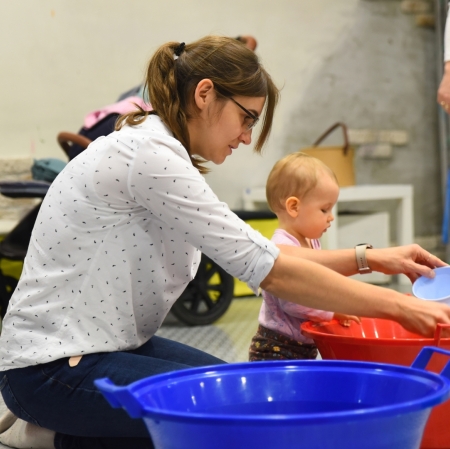 A woman and a girl are sitting at a blue and red bowl sifting various products