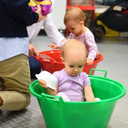 little girls sitting in large green and red bowls engaging in sensory activities