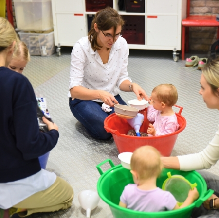 women sitting on the floor, and children sitting in green and red bowls