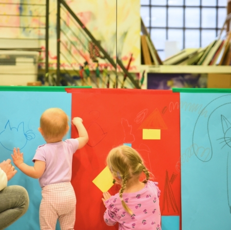 two girls are painting on red and blue cardboards glued to the wall