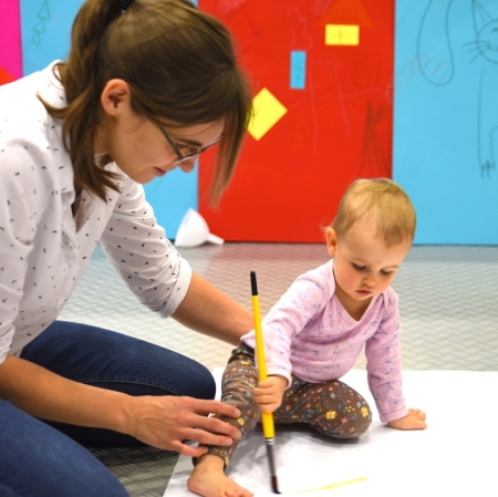 a woman and a girl sitting on the floor paint with brushes