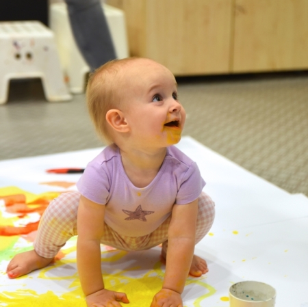 a little laughing girl smearing yellow paint with her hands