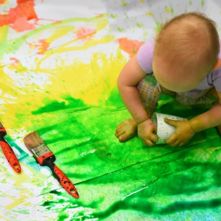 a girl sitting on a cardboard painted with splashes of colorful paints