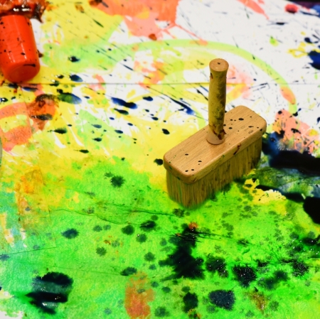 a large paintbrush standing in the middle of splashes of colorful paints