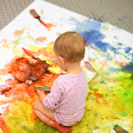 a girl sitting on a cardboard painted with splashes of colorful paints