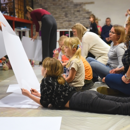 the educator hands out large cardboard boxes to children in the workshop space