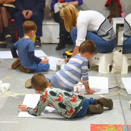 children sitting on the floor and drawing in the background adults sitting in front of a gray wall, three in the foreground