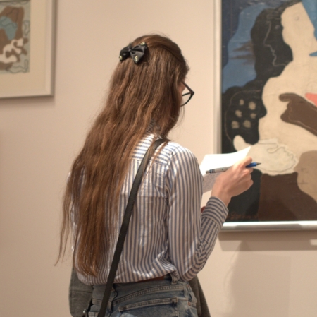 The girl stands with a piece of paper in front of the painting.