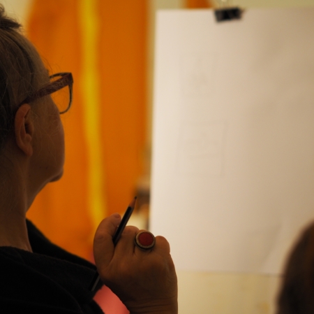 face of a woman with glasses looking at a blank sheet of paper and holding a brush