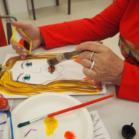 kobieta w czerwonym swetrze malująca posrtret pędzlem, obok leża farby i paleta