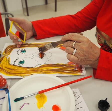 a woman in a red sweater painting a portrait with a brush, paints and a palette lying next to her