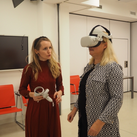 dwie stojące kobiety, jedna z nich ma na sobie okulary VR