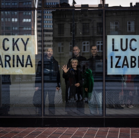 Artystka Jadwiga Sawicka oraz Marin Polak, Łukasz Ogórek, Tomasz Załuski, widziany przez szybę, na której znajdują się prace artyski