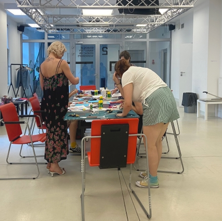 kilka osób stojących lub siedzących przy stole w sali warsztatowej