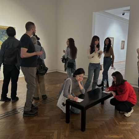 several people in the exhibition space. some write, others stand