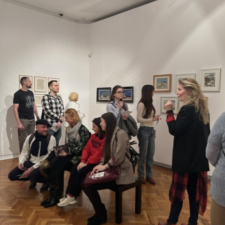 several people in the exhibition space. they are sitting on a dark bench in the middle of the room