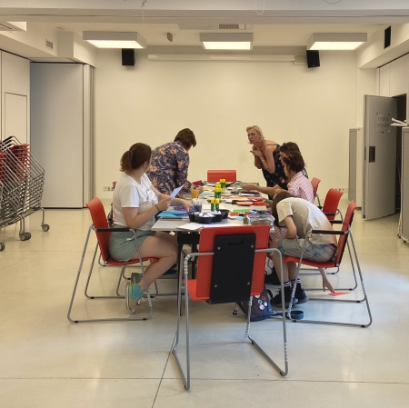 kilka osób stojących lub siedzących przy stole w sali warsztatowej