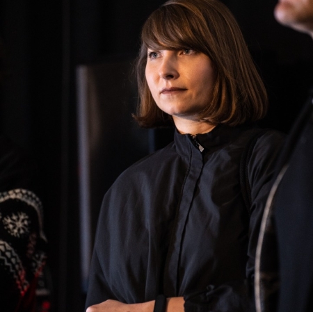 Członkini jury Małgorzata Szymankiewicz stoi w czarnym ubraniu, na ciemnym tle. Ma brązowe włosy do ramion i grzywkę.