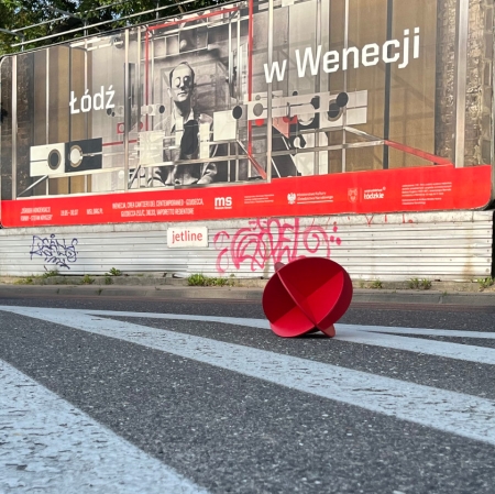 Zdjęcie plakatu billboard, na pierwszym planie czerwony kulisty obiekt leżący na jezdni