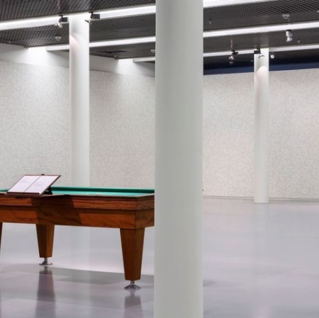 Fragment espozycji z widocznymi filarami, stołem do gry oraz w tle widocznymi ścianami wypełnionymi kośćmi.