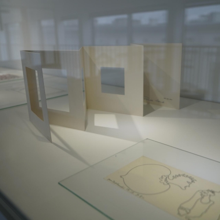 Fragment of the exhibition. A vertically arranged, concertina-fold postcard with cut out squares of various sizes.