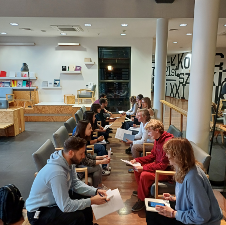 Kilkanaście osób siedzi obok siebie i pisze na kartkach