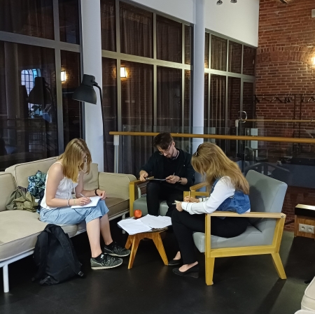 Kilka osób siedzi przy stole i pisze na kartkach