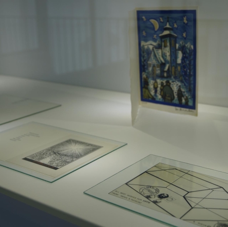 Fragment of the exhibition. Two lying cards with geometric patterns. In the background there is a vertically placed card with a watercolor landscape.