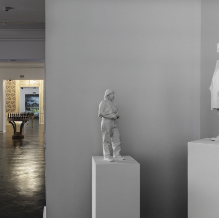 Two sculptures standing on stands, exhibition visible in background