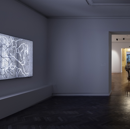 przestrzeń wystawy. po lewej stronie widoczny druk soczewkowy. na wprost widok na stół, na którym stoją miniaturowe pomniki.