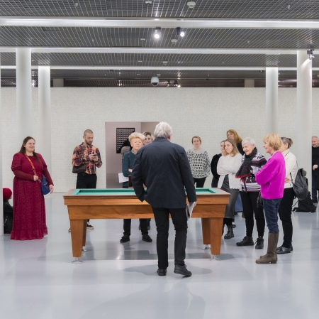 Grupa osób w przestrzeni wystawy, zgromadzona wokół stołu do gry