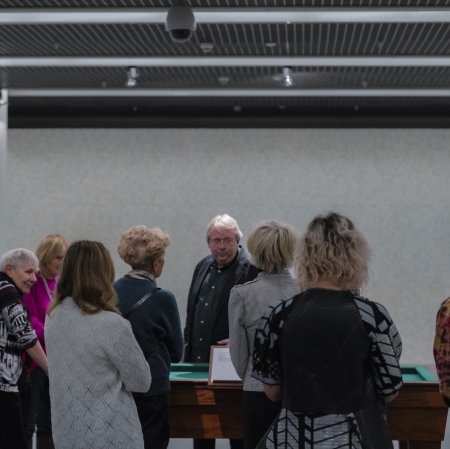 Grupa osób stojących wokół stołu do gry. W tle po sciany wypełnione kośćmi. Po obu stronach filary.