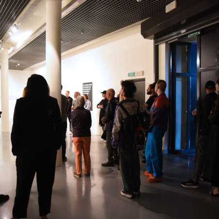 Grupa osób w przestrzeni wystawy podczas oprowadzania kuratorskie Pawłą Polita