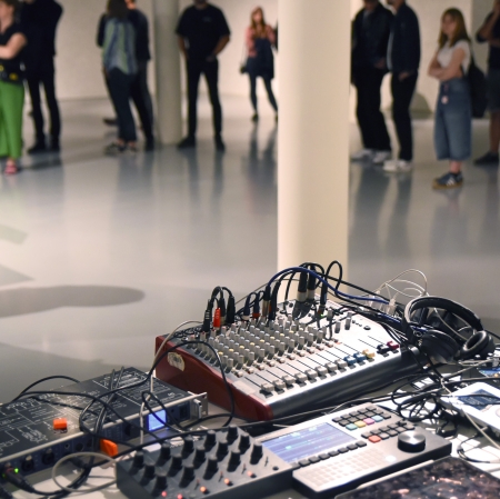 Na pierwszym planie konsola DJ. W tle duża grupa osób.