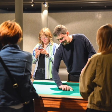 Grupa osób stojąca wokół stołu do gry i rzucająca kośćmi.