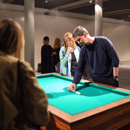 Grupa osób stojąca wokół stołu do gry i rzucająca kośćmi.