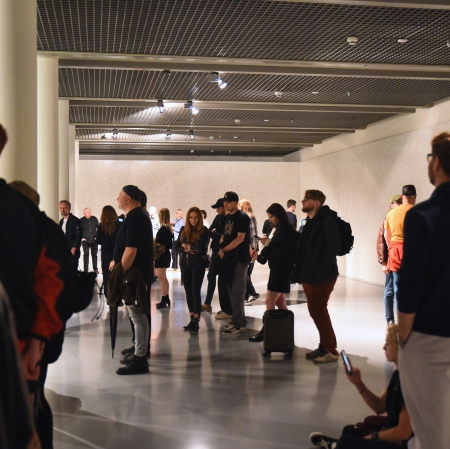 Duża grupa osób w przyciemnionej sali wystawowej.