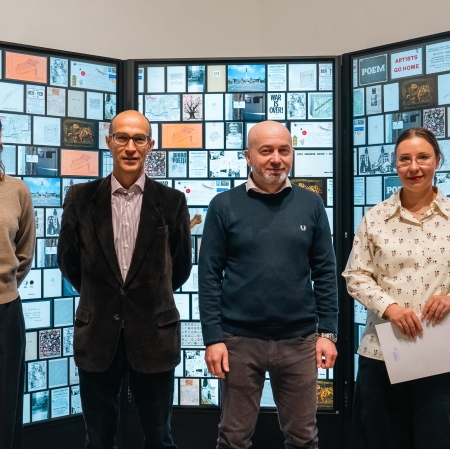 cztery osoby stoją na tle ekranów, na których wyświetlane są zdjęcia.