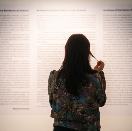 kobieta widoczna od tyłu. przed nią ściana, na której widnieje tekst.