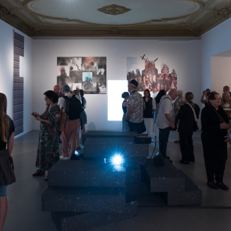 Several dozen people in the exhibition space. A harsh light in the center. 