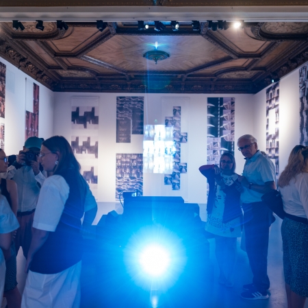 Dozens of people in the exhibition space. In the center, harsh, blinding light.