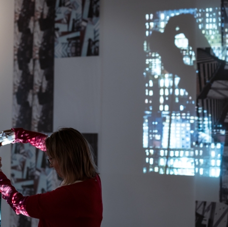 A woman takes a picture with her camera in the exhibition space. Her shadow is reflected on the wall.