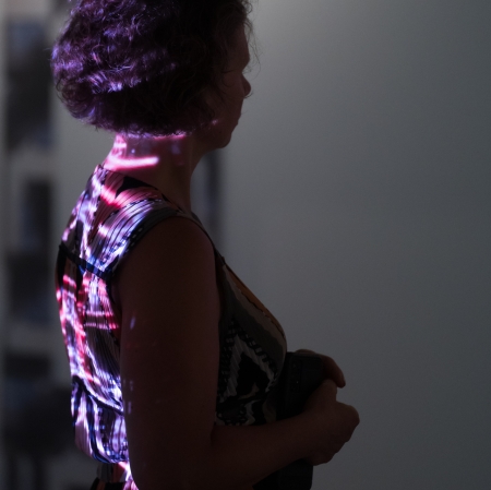 A fragment of light illumination is reflected on the back of a woman standing in profile. 