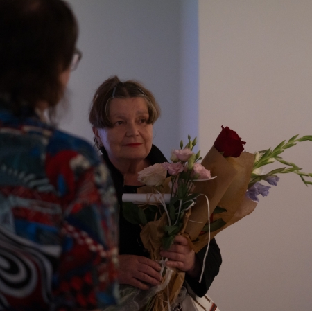In the center - a woman with flowers. In the right edge of the photo - hands holding a phone. On the left - a woman visible from behind.