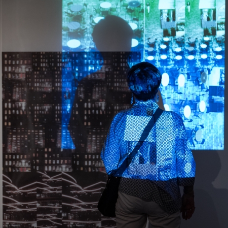 A woman standing with her back. A fragment of light illumination is reflected on her back. Her shadow is reflected on the wall.