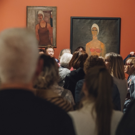 Duża grupa osób w przestrzeni wystawy. W tle widoczne wielkoformatowe portrety.