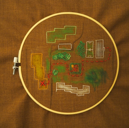 materiał umieszczony w tamborku, na którym wyszyte zostały różne kształty reprezentujące mapę oraz wyszyta na czerwono ścieżka