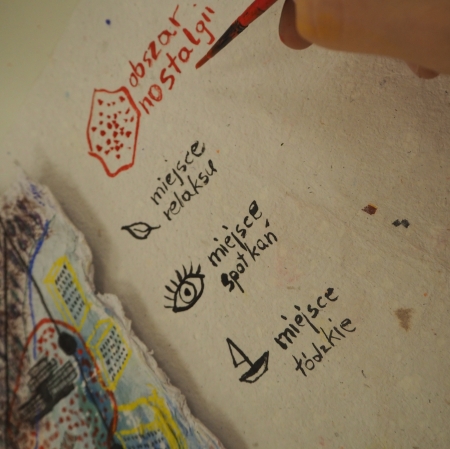 dłoń trzymająca pędzelek i zapisująca na kartce napis obszar nostalgii